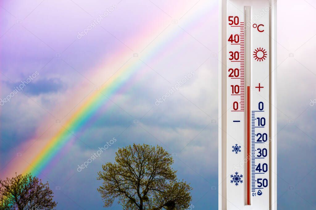 The thermometer on the background of sky with a rainbow shows 15 degrees of heat