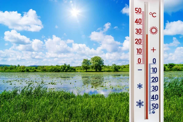 Güneşli bir günde, yaz manzarasının arka planındaki termometre 30 derece sıcaklığı gösteriyor. Yaz sıcağı