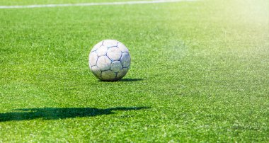 Stadyumun yeşil çimlerinde futbol topu ve güneşli havada bir futbolcunun gölgesi.