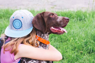 Kız, Alman Shorthair Pointer cinsinden bir köpeğe sarılıyor. Çocuk ve köpek arkadaşlar.
