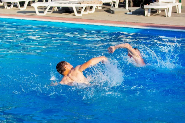 İki adam havuzda yüzüyor. Tatil köyünde yaz tatili