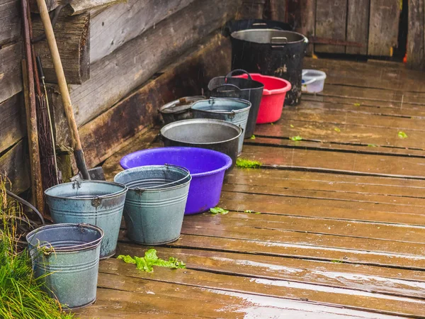 Agricultural equipment under the house in rainy weather. Bucket and bowl on a wood floor