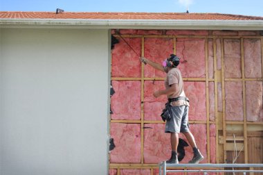 AUCKLAND - APR 18 2018:Builder removing old fiberglass wall insulation.Home improvement companies traded asbestos insulation for fiberglass after finding out the harmful effects asbestos has on lungs. clipart