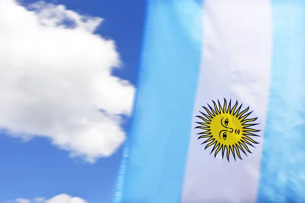 The Flag of Argentina with the  Sun of May symbol against white clouds and blue sky.