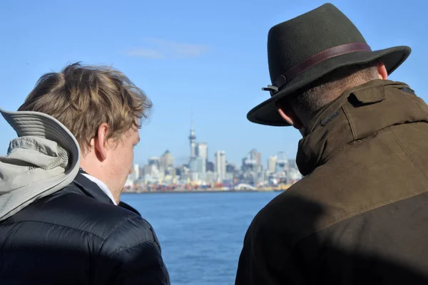 两名男性游客的后景色在一艘渡轮上旅行 看着新西兰的奥克兰城市天际线 每年有近350万人访问新西兰 — 图库照片