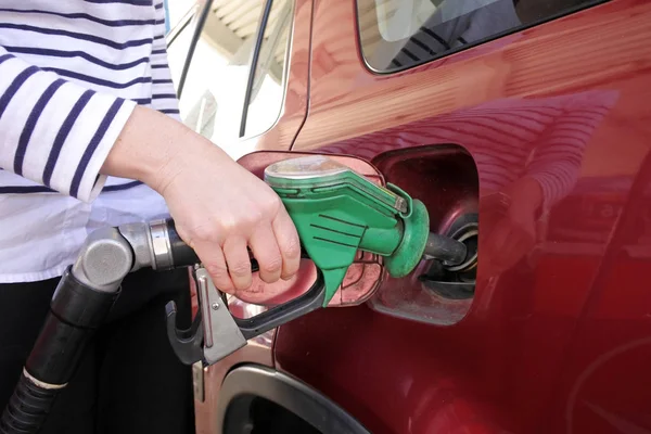 Woman using a gas pump nozzle fulling a car in a gas station.