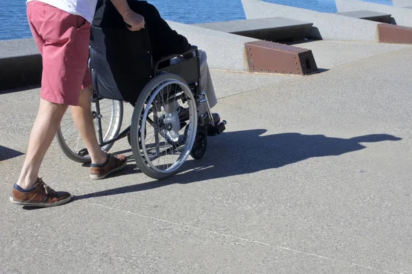 Pessoa empurrando um homem idoso adulto em uma cadeira de rodas ao ar livre — Fotografia de Stock