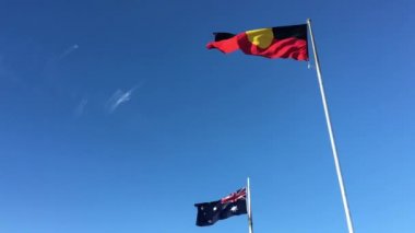 Avustralya Aborjin Bayrağı açık mavi gökyüzü altında dalgalanıyor.