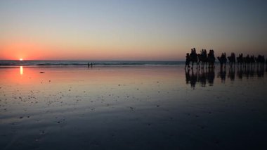 Cable Beach Broome Batı Avustralya 'da deve sürüşünde tanınmayan turistlerin silueti..