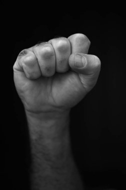 Siyah arka planda izole edilmiş erkek yumruğu. Sıkışmış yumruk, dayanışma ve desteğin bir sembolüdür. Aynı zamanda birlik, güç, meydan okuma veya direnişi ifade etmek için bir selam olarak kullanılır..