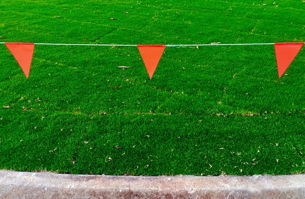 一条红色三角形警告旗挂在金属丝上 以保护新安装的天然青草地毯 — 图库照片