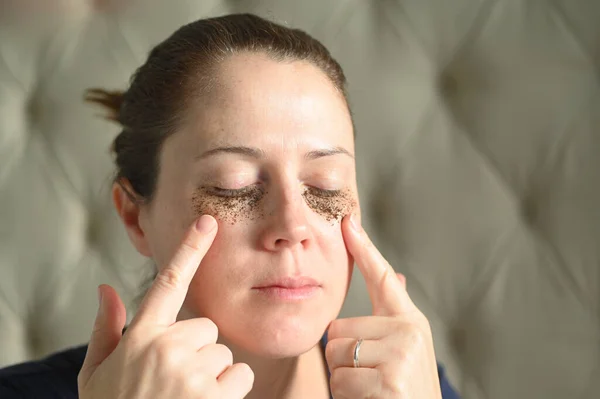 Adult woman (age 35-40)  relaxing at home with coffee grounds on her face to help to clear away dead skin cells and unclog the pores.