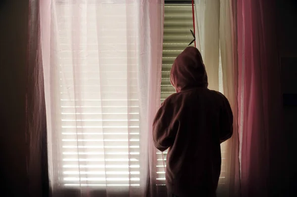 家庭内暴力のパーカーの被害者を着ている若い女の子は彼女のベッドルームの窓の外を見る — ストック写真
