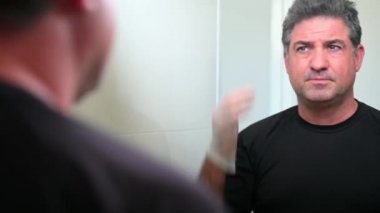 Yetişkin bir adam (40-50 yaş) ev banyosunda saçını boyuyor.