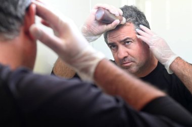 Yetişkin bir adam (40-50 yaş) aynada banyoda saçını boyuyor..