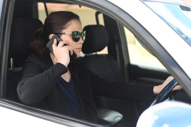 Yetişkin kadın (30-40 yaş) araç kullanırken cep telefonu kullanıyor.