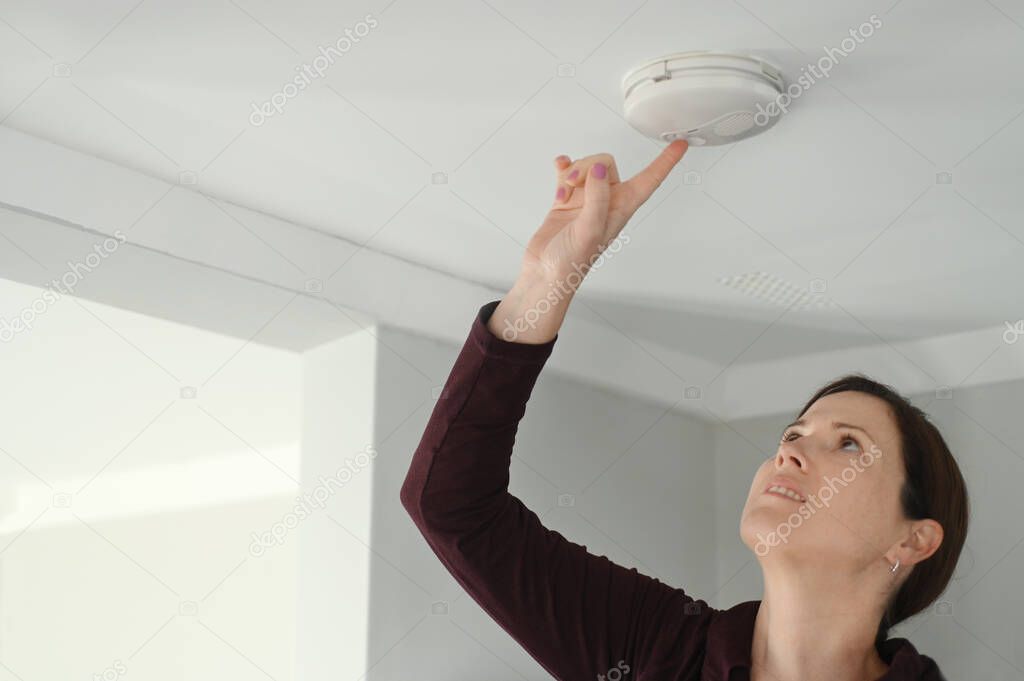 Young adult woman (age 25-35) checking fire alarm at home.