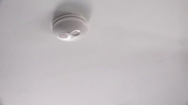 Genç yetişkin kadın (25-35 yaş) evde yangın alarmını kontrol ediyor.