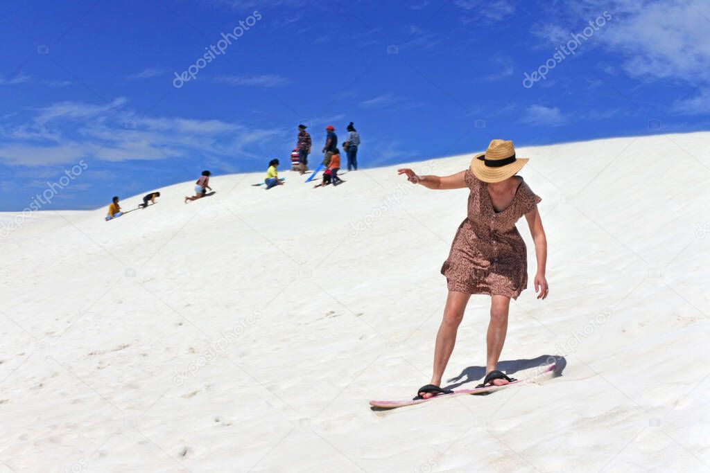 Adult Australian woman sliding down with a snowboard on Lancelin sand dunes near Perth in Western Australia.
