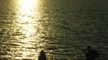 Çok hoş bir siluet adam sahilde gün batımında akıllı telefon fotoğrafı çeken kadın..