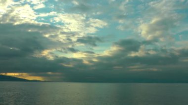 Gün batımında sessiz bir ada. Yumuşak bulutların yavaşça solan güneşe doğru hareket ettiğini gösteriyor. Güneş 'in altın-turuncu ışınları okyanusa yansıyor..