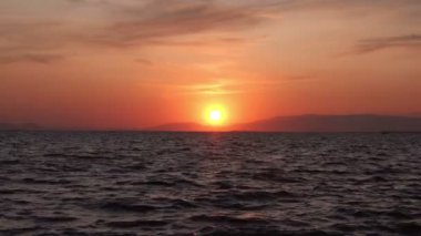 Gün batımında sessiz bir ada. Yumuşak bulutların yavaşça solan güneşe doğru hareket ettiğini gösteriyor. Güneş 'in altın-turuncu ışınları okyanusa yansıyor..