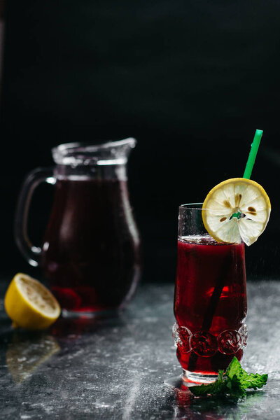 Свежий вишневый сок, мята, лимон и лед на темном фоне, вид сбоку, пространство для копирования

