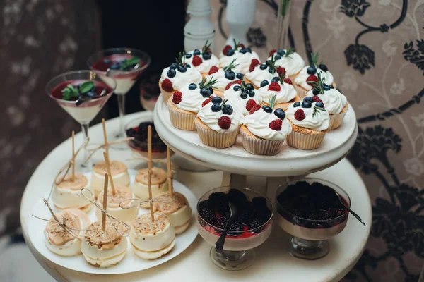 Sweet table. A plates of cakes and muffins with cream with berries. Table with sweets, candy, buffet. Dessert table for a party goodies. Close up. party reception, decorated in restaurant. candy bar