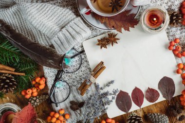 Şık düz ahşap arka plan üzerinde görünümü ekose desenli kazak ve sonbahar yaprakları çay ile yatıyordu. Sonbahar ya da kış konsepti. 