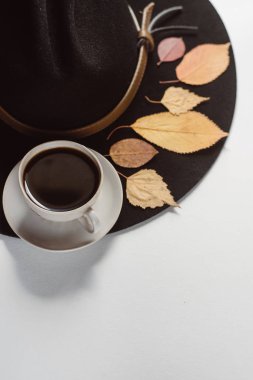 Beyaz bir arka plan üzerine bir fincan kahve ve bir şapka ile sonbahar yaprakları