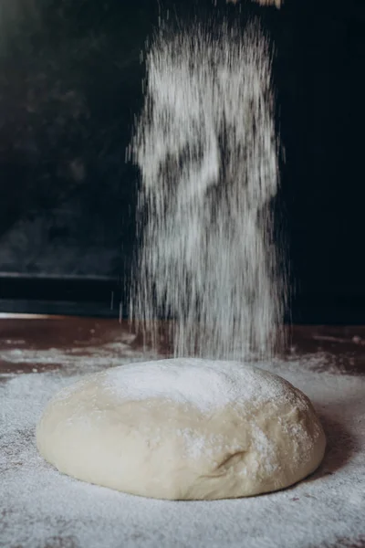 Ball of raw dough sprinkled with flour on rustic wooden counter