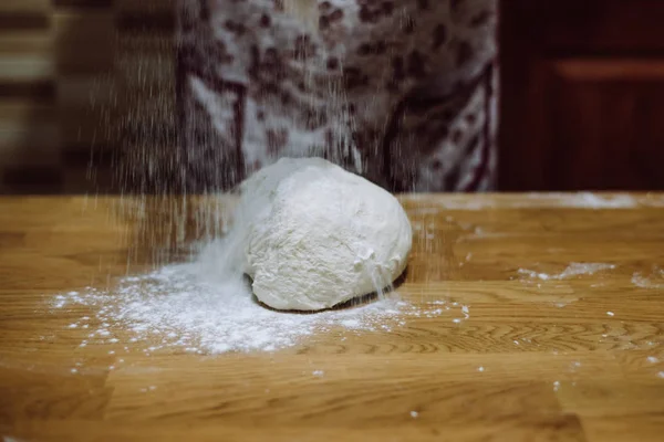 Ball of raw dough sprinkled with flour on rustic wooden counter