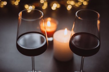 İki kadeh şarap kırmızı duran mum ve çelenk karanlık bir tablo