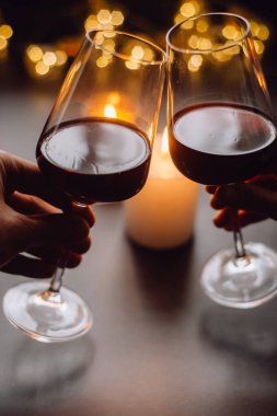 İki kadeh şarap kırmızı arka plan mum ve çelenk elinde 