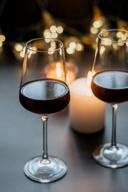 İki kadeh şarap kırmızı duran mum ve çelenk karanlık bir tablo