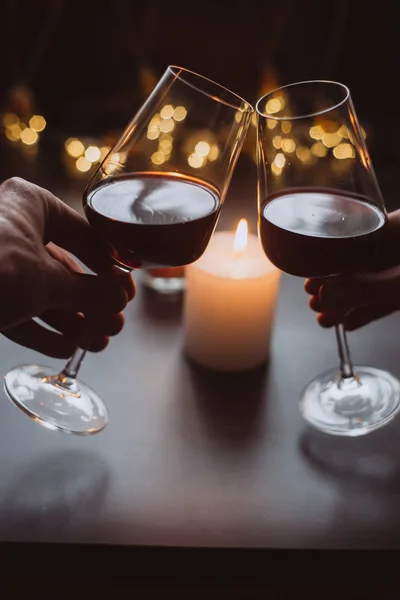 Two glasses of wine  red in hand on the background candle and  garlands