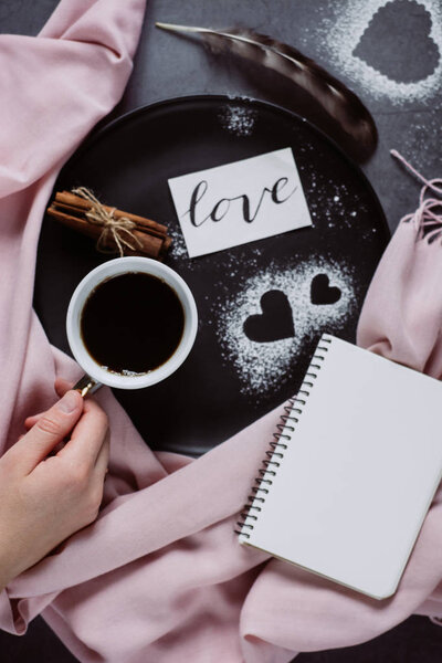 День Святого Валентина. Рука держит чашку кофе, ноутбук, шарф, корицу и сердце на сером столе сверху в плоском стиле
.