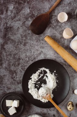 Malzemeler ve pişirme için mutfak eşyaları. Kaşık un, yemekler, yumurta, tereyağı tuz ve gri arka plan üzerinde oklava ile. Düz yatıyordu. Metin alanı