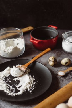 Malzemeler ve pişirme için mutfak eşyaları. Kaşık un, yemekler, yumurta, tereyağı tuz ve gri arka plan üzerinde oklava ile. Düz yatıyordu. 