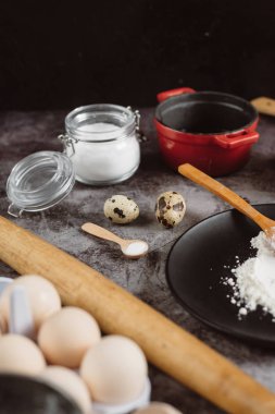 Malzemeler ve pişirme için mutfak eşyaları. Kaşık un, yemekler, yumurta, tereyağı tuz ve gri arka plan üzerinde oklava ile. Düz yatıyordu. 