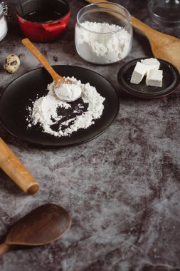 Malzemeler ve pişirme için mutfak eşyaları. Kaşık un, yemekler, yumurta, tereyağı tuz ve gri arka plan üzerinde oklava ile. Düz yatıyordu. Metin alanı