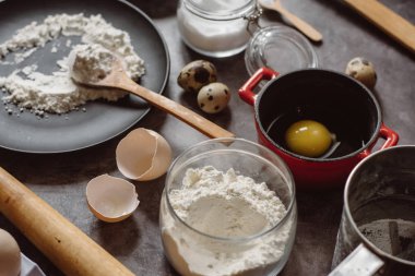 Malzemeler ve pişirme için mutfak eşyaları. Kaşık un, yemekler, yumurta, tereyağı tuz ve gri arka plan üzerinde oklava ile. Düz yatıyordu. 