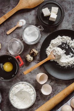 Malzemeler ve pişirme için mutfak eşyaları. Kaşık un, yemekler, yumurta, tereyağı tuz ve gri arka plan üzerinde oklava ile. Düz yatıyordu. 