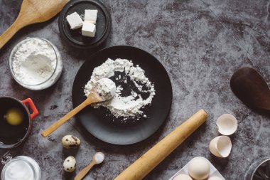 Malzemeler ve pişirme için mutfak eşyaları. Kaşık un, yemekler, yumurta, tereyağı tuz ve gri arka plan üzerinde oklava ile. Düz yatıyordu. Metin alanı