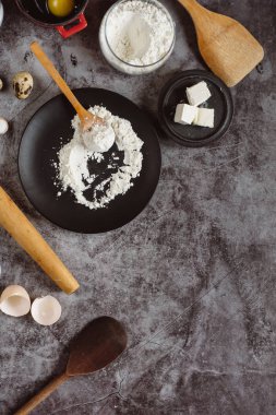 Malzemeler ve pişirme için mutfak eşyaları. Kaşık un, yemekler, yumurta, tereyağı tuz ve gri arka plan üzerinde oklava ile. Düz yatıyordu. Metin alanı