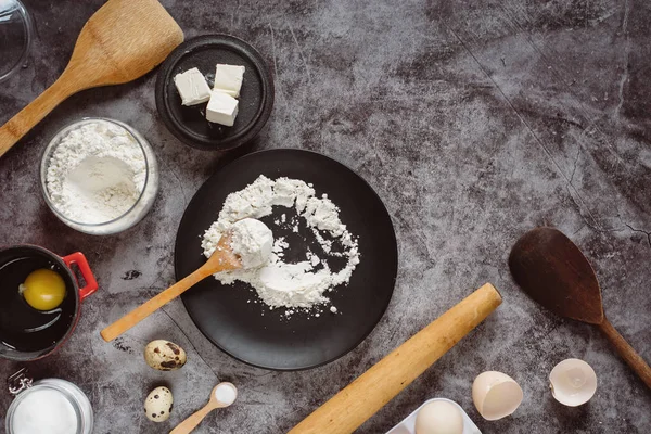 Malzemeler ve pişirme için mutfak eşyaları. Kaşık un, yemekler, yumurta, tereyağı tuz ve gri arka plan üzerinde oklava ile. Düz yatıyordu. Metin alanı