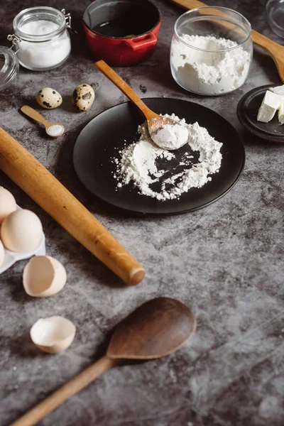 Malzemeler ve pişirme için mutfak eşyaları. Kaşık un, yemekler, yumurta, tereyağı tuz ve gri arka plan üzerinde oklava ile. Düz yatıyordu. Metin alanı