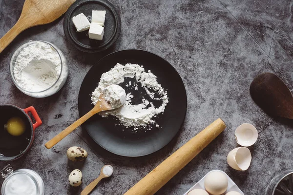 Malzemeler ve pişirme için mutfak eşyaları. Kaşık un, yemekler, yumurta, tereyağı tuz ve gri arka plan üzerinde oklava ile. Düz yatıyordu. Metin alanı