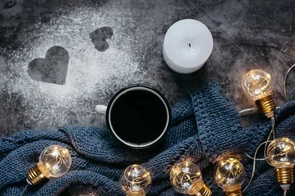 Cup of coffee , candle, notebook, pen and warm woolen sweater , decorated with led lights on gray table.Winter  concept. Flat lay, top view. Valentines day.