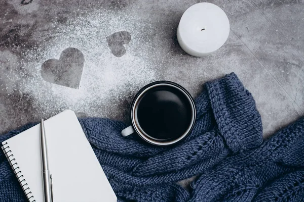 Cup of coffee , candle, notebook, pen and warm woolen sweater  on gray table.Winter concept. Flat lay, top view. Valentines day.